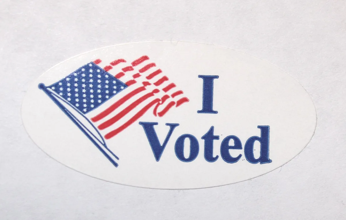 A close-up of a white oval sticker featuring a stylized American flag with red stripes and a blue canton with white stars…