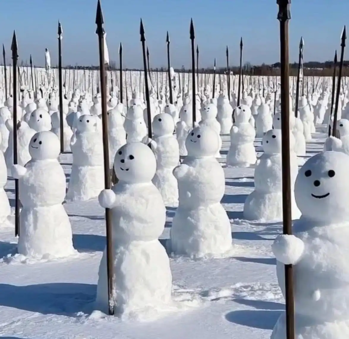 A vast field of snowmen, each holding a long spear with a pointed tip, arranged in neat rows under a clear blue sky. The…