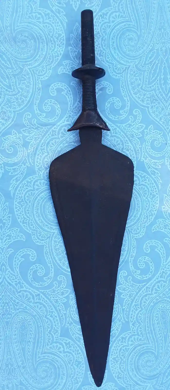A dark, blunt-ended spear-like weapon with a thick, tapered blade and a simple cylindrical handle rests vertically on a…