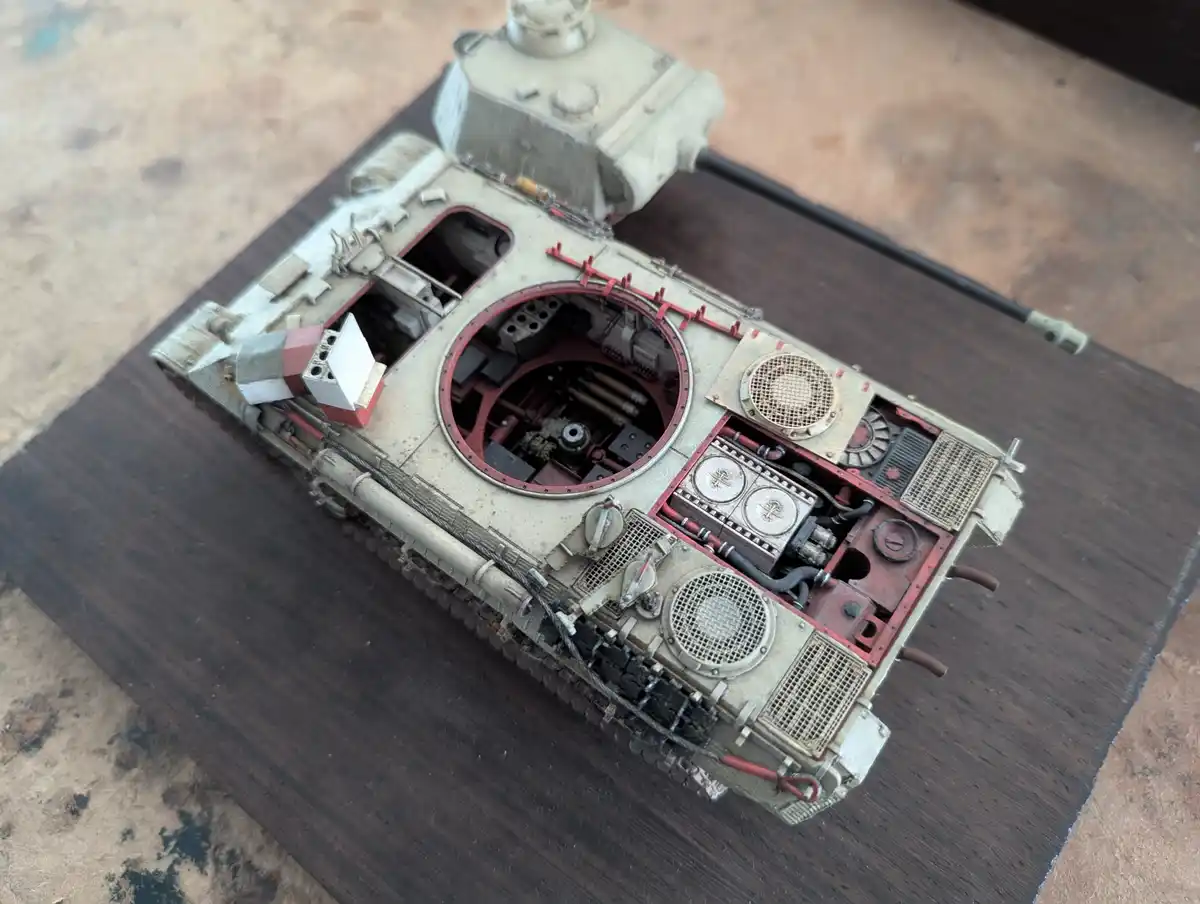 A highly detailed, weathered scale model of a military tank is shown with its top and side panels removed, revealing…
