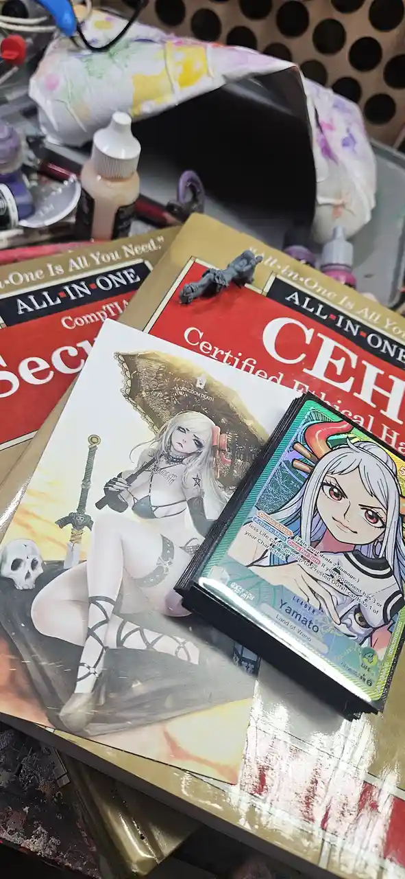 A cluttered desk holds 'All-in-One' certification books for CompTIA Security+ and CEH, alongside a 'Kingdom Death' game card…