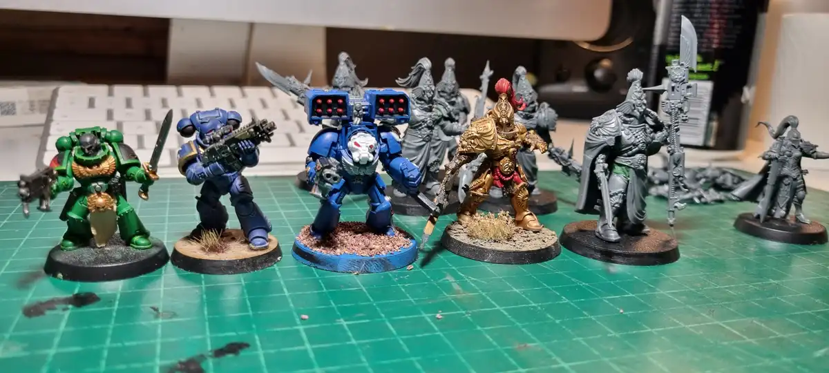 A row of painted and unpainted miniature fantasy and sci-fi war figurines, including green-armored, blue-armored, and…