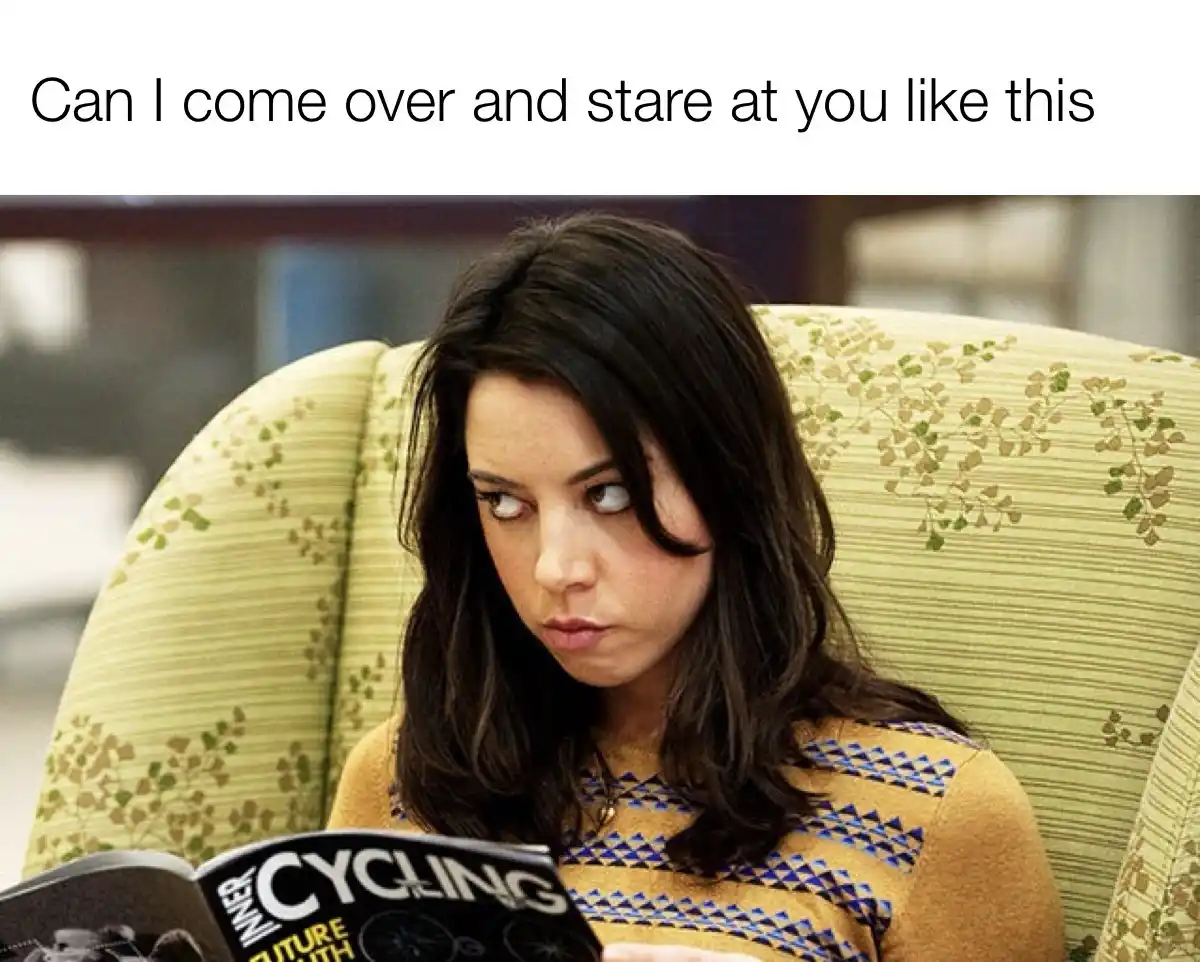 A woman with dark hair sits in a patterned green armchair, holding an open magazine titled 'CYCLING'. She stares intently…