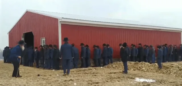 A composite image shows a long line of people in historical Civil War-era Union Army uniforms standing outside a red barn…