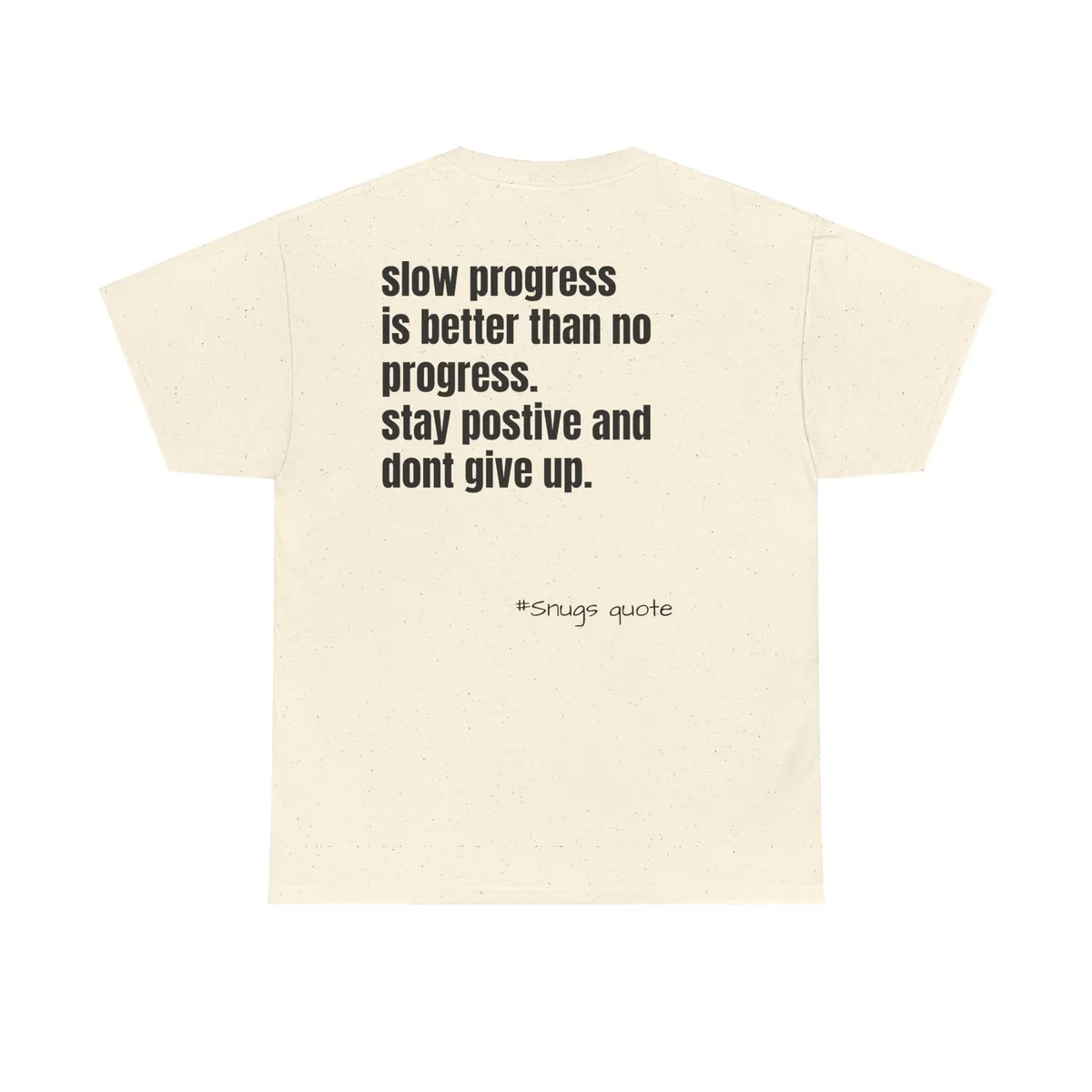The image shows the back of a cream-colored, speckled t-shirt with black text. The main text reads 'slow progress is better…