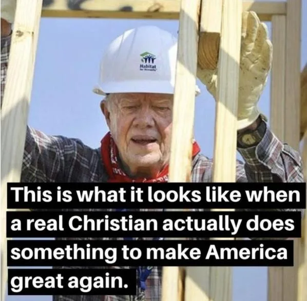 An elderly man wearing a white Habitat for Humanity hard hat and work gloves is shown holding wooden framing beams on a…