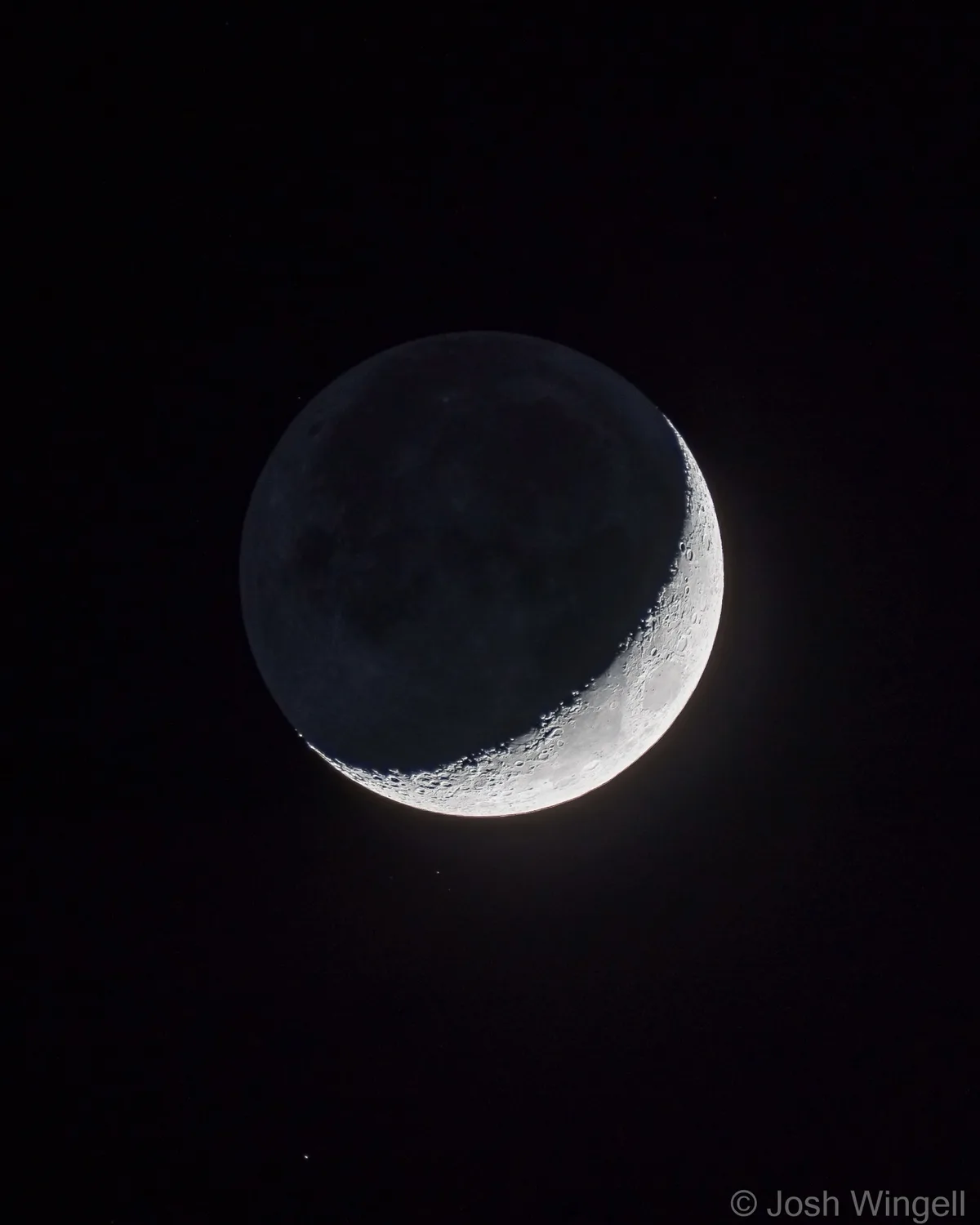 A close-up photograph of a crescent moon against a black night sky, showing detailed craters on the illuminated portion. The…