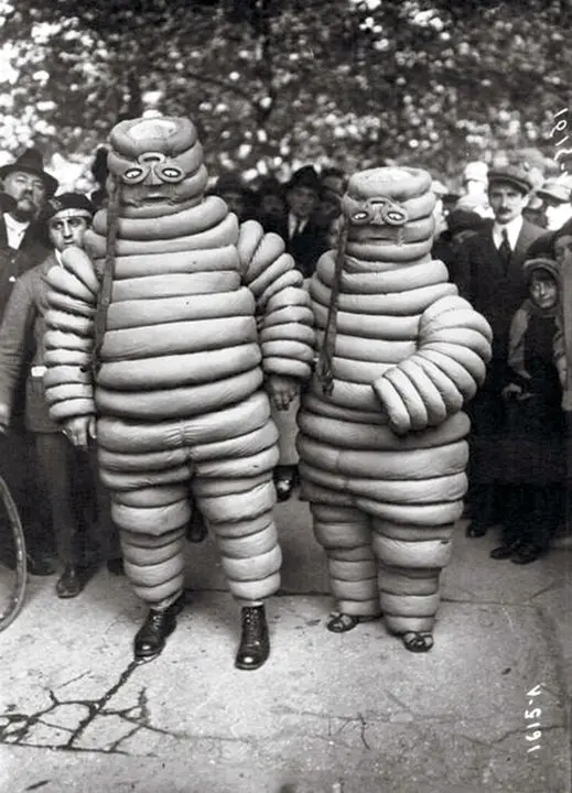 Two men in large, segmented, inflatable costumes resembling cartoonish aliens or creatures stand side by side on a cracked…