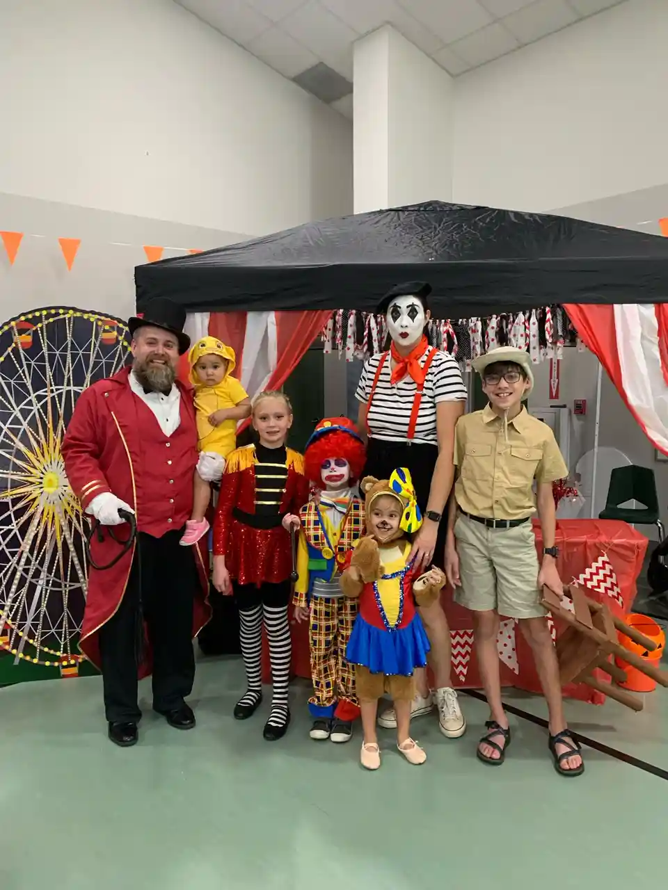 A group of six people, including adults and children, pose together in a room decorated for a circus-themed event. They are…