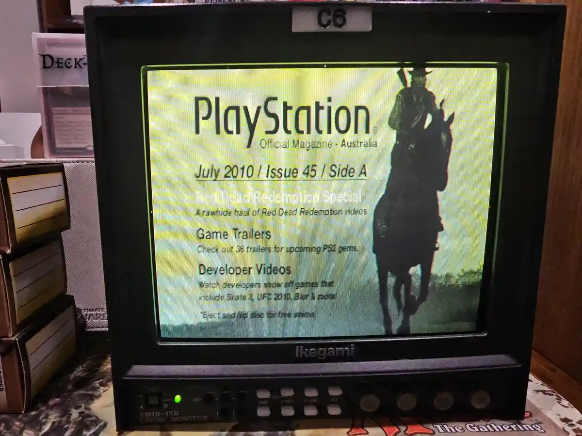 An old Ikegami TM10-17R color monitor displays the July 2010 cover of PlayStation Official Magazine Australia, featuring a…