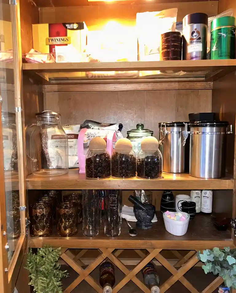 A well-lit wooden cabinet with glass doors displays three shelves filled with tea and coffee products. The top shelf holds…
