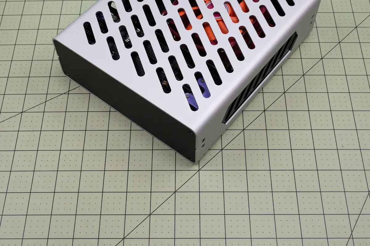 A silver computer case with a perforated top sits on a green grid mat, revealing colorful internal components through the…