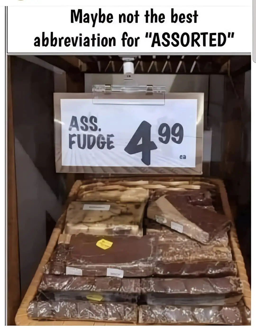 A store display of assorted fudge bars stacked in a wooden tray, with a handwritten sign above reading "ASS. FUDGE 4.99 ea"…