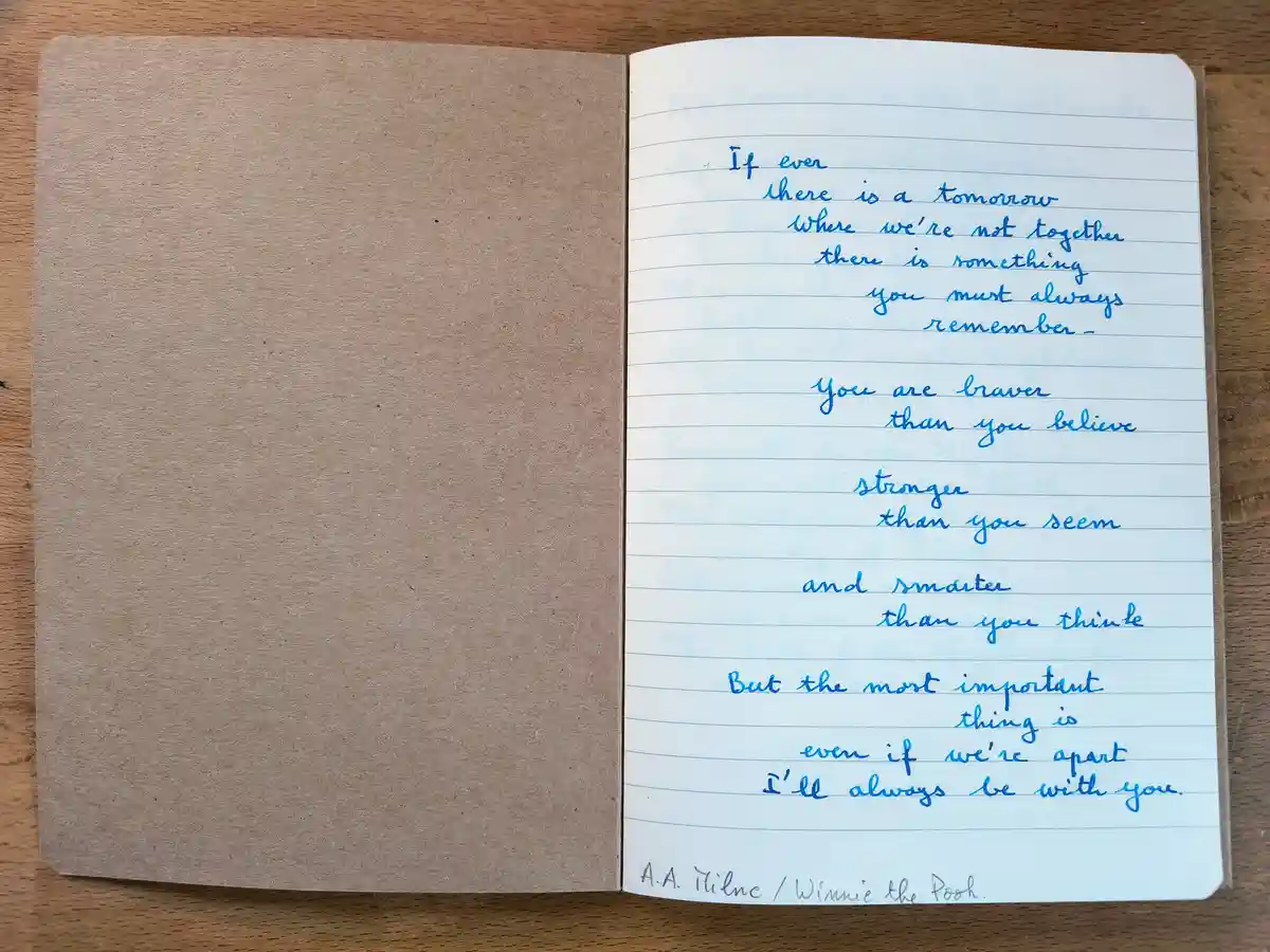 A handwritten note in blue ink on lined paper inside a brown notebook, placed on a wooden surface. The note is a sentimental…