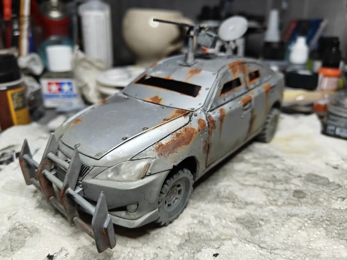 A heavily modified, rusted, and armored model car with a spiked front bumper, mounted weapon, and satellite dish sits on a…