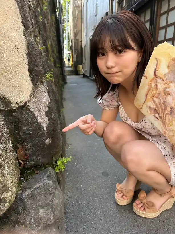 A young woman crouches in a narrow alleyway, pointing at a small crab hiding in the crevice of a stone wall. She holds a…