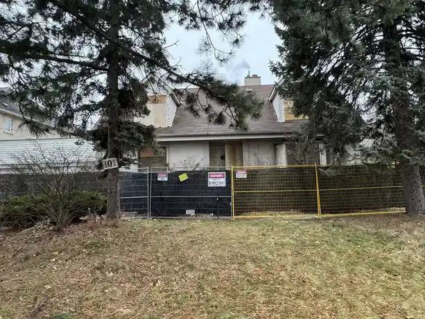 A house is surrounded by a yellow and black construction fence with multiple 'DANGER' signs, including one that reads…