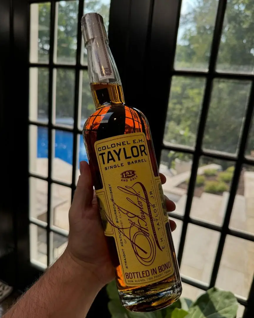 A hand holds a bottle of Colonel E.H. Taylor Single Barrel bourbon whiskey, labeled 'Bottled in Bond' and '151 and Only', in…