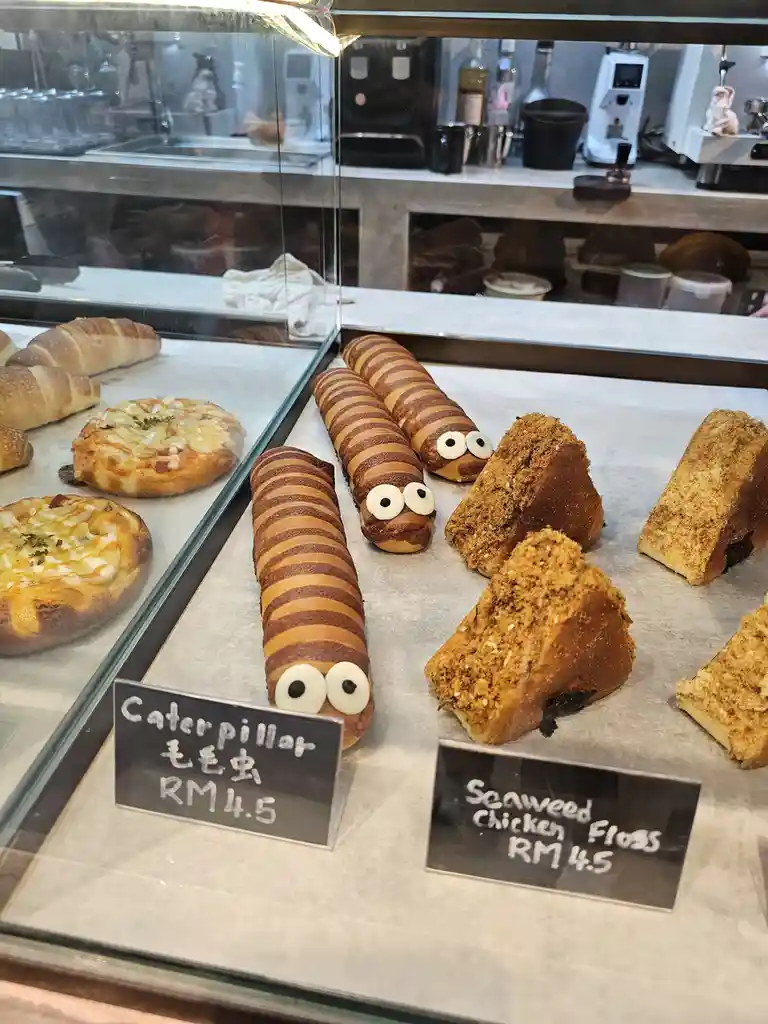 A bakery display case shows several pastries, including three striped, caterpillar-shaped bread rolls with googly eyes…