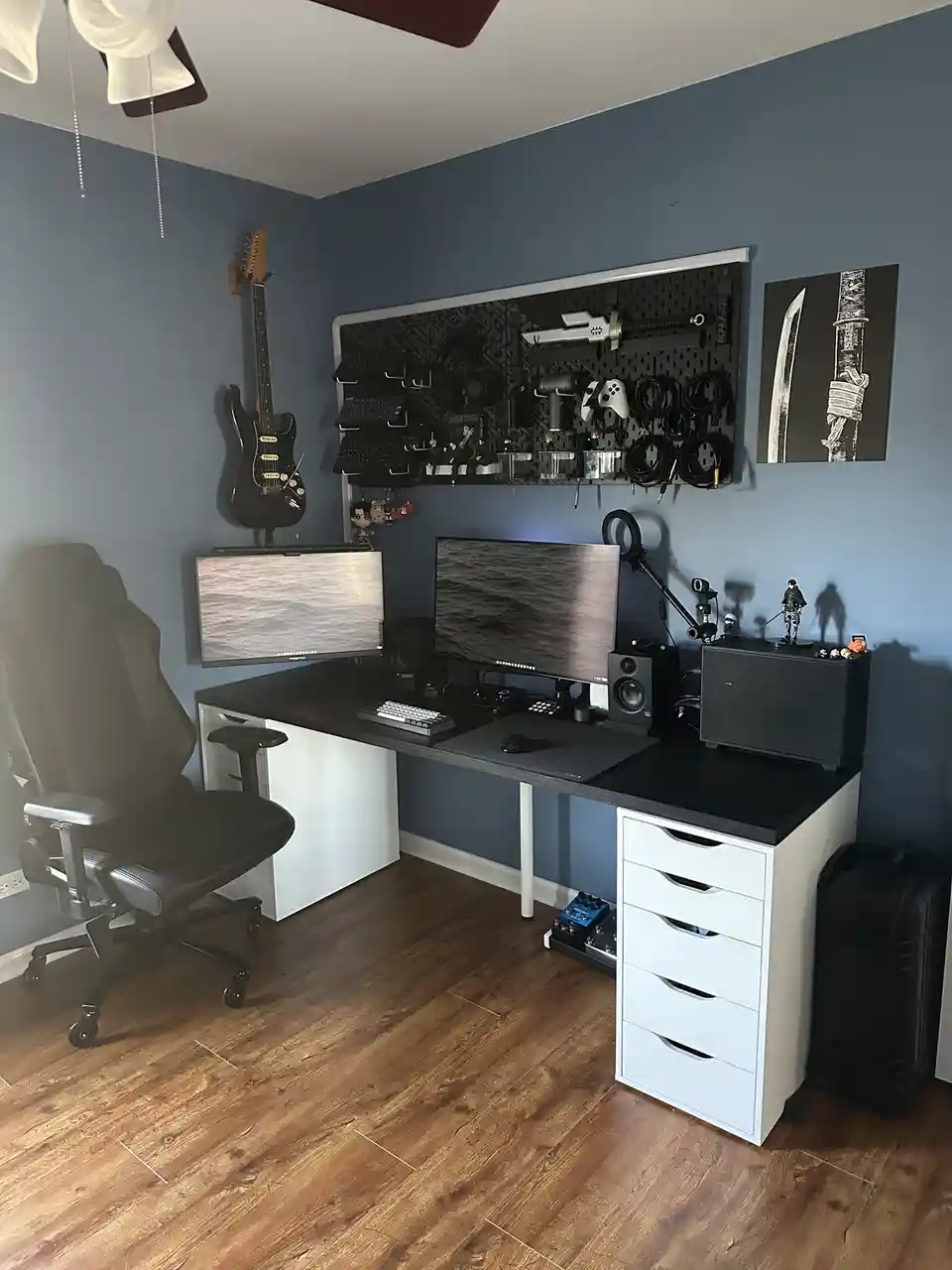 A meticulously organized gaming or streaming setup with dual monitors, a high-end ergonomic chair, and a large wall-mounted…
