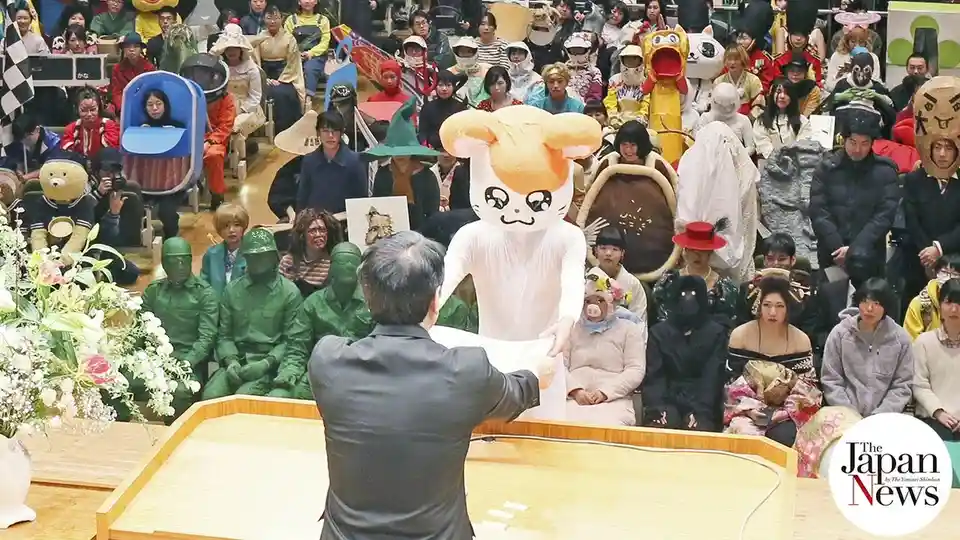 a man in a formal suit stands at a wooden podium facing a large audience of people dressed in wildly varied costumes…
