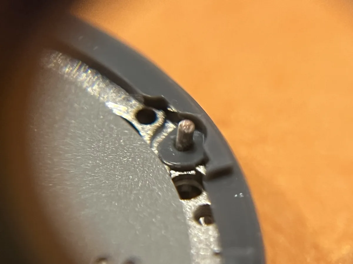 A close-up photo shows the internal mechanism of a watch, with a small screw visible in a black plastic casing against an…