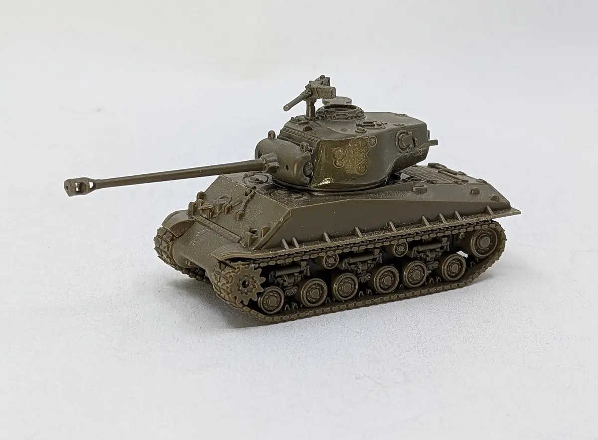 A small, olive-drab model of a military tank with a long cannon and detailed tracks sits on a plain white surface. The…