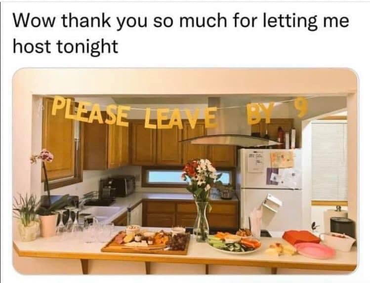 A kitchen counter is set with appetizers, drinks, and flowers, with a yellow banner reading 'PLEASE LEAVE BY 9' strung…