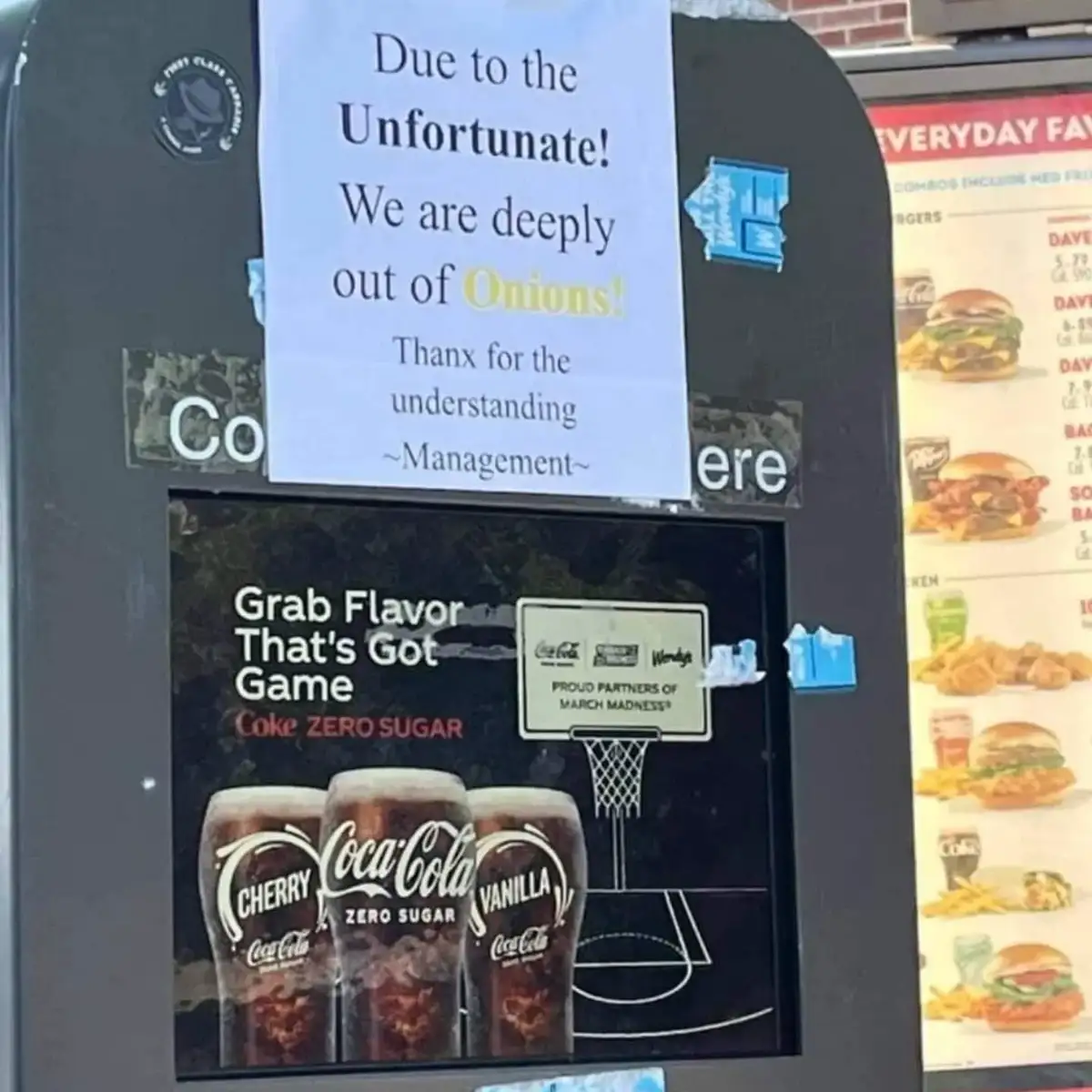 A handwritten sign taped to a fast-food restaurant's menu board announces they are out of onions, using the word…