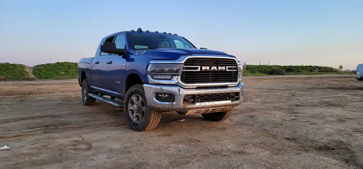 A blue Ram 2500 pickup truck is parked on a dirt lot, its front bumper and tires covered in mud, suggesting recent off-road…