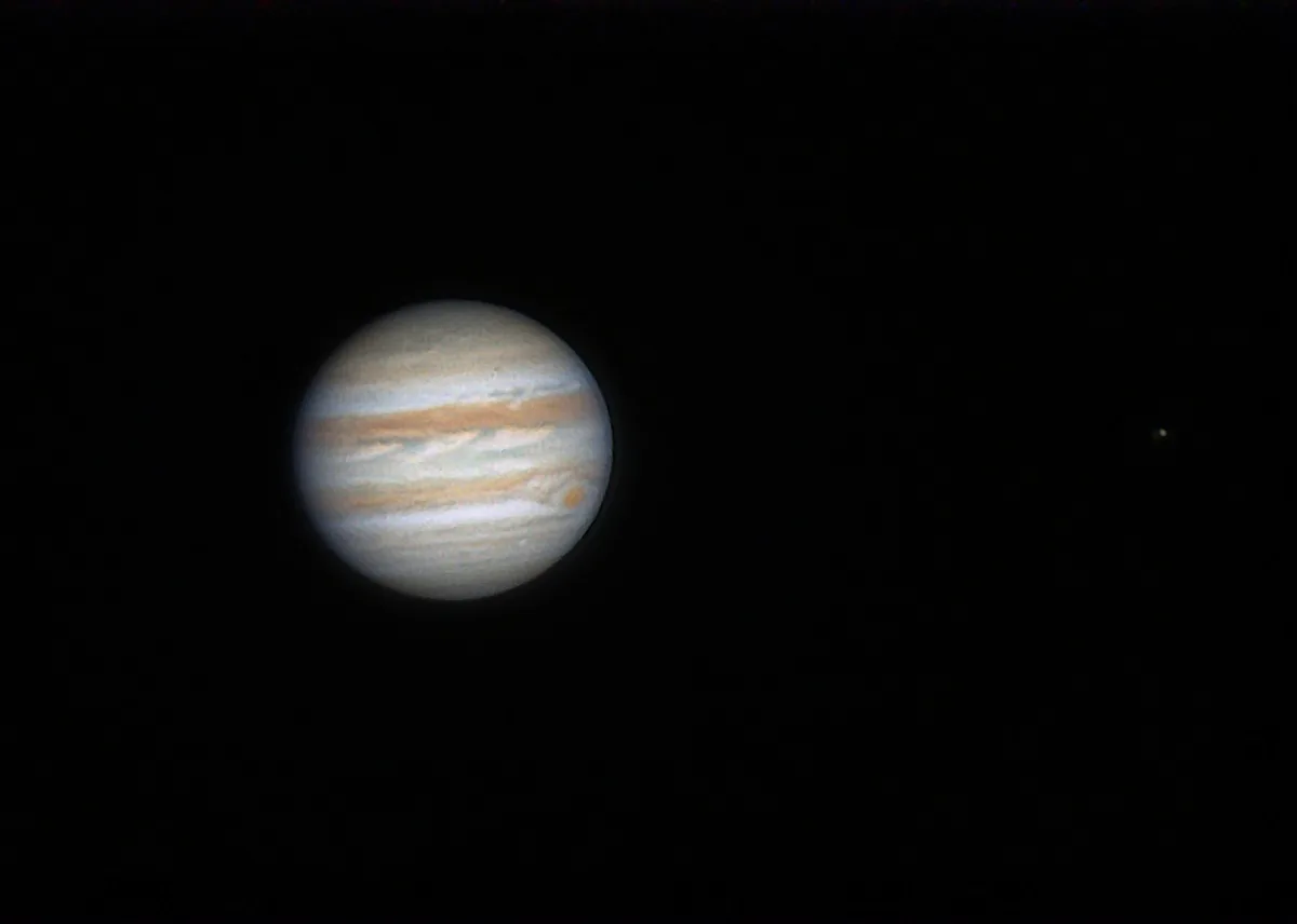 A low-resolution image shows the planet Jupiter with its characteristic swirling bands of white, orange, and brown, set…