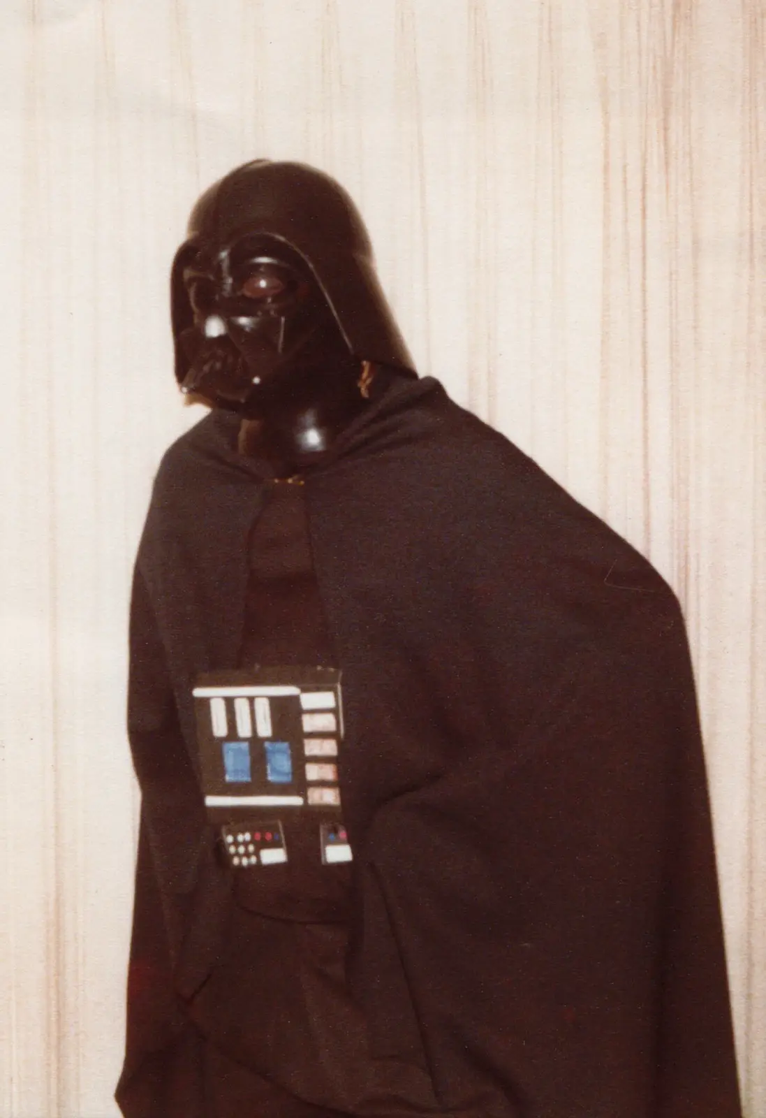 A person wearing a Darth Vader helmet and a black hooded sweatshirt with a printed chest panel resembling Vader's armor…