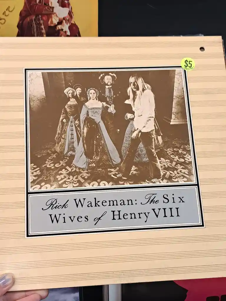A sepia-toned album cover for Rick Wakeman's 'The Six Wives of Henry VIII' shows a man in 1970s casual attire standing…