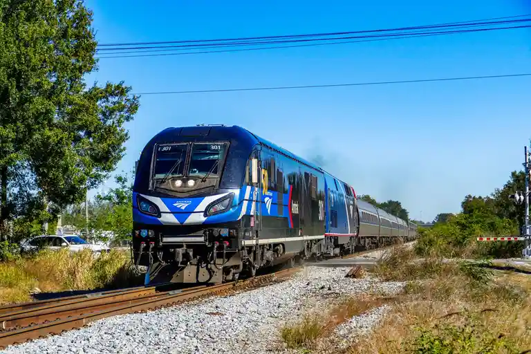 An Amtrak train, numbered 301 and featuring a blue and silver livery with a '50' anniversary logo, travels along tracks…