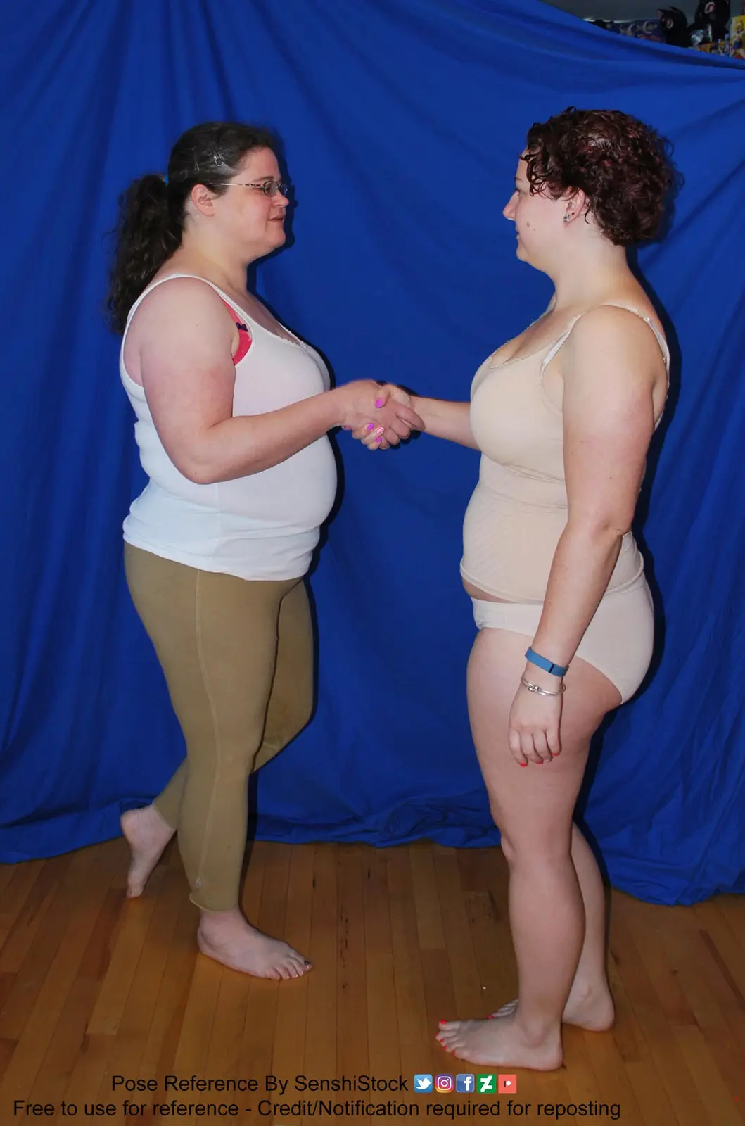 Two women stand side-by-side against a blue backdrop, shaking hands while facing each other. The woman on the left wears a…