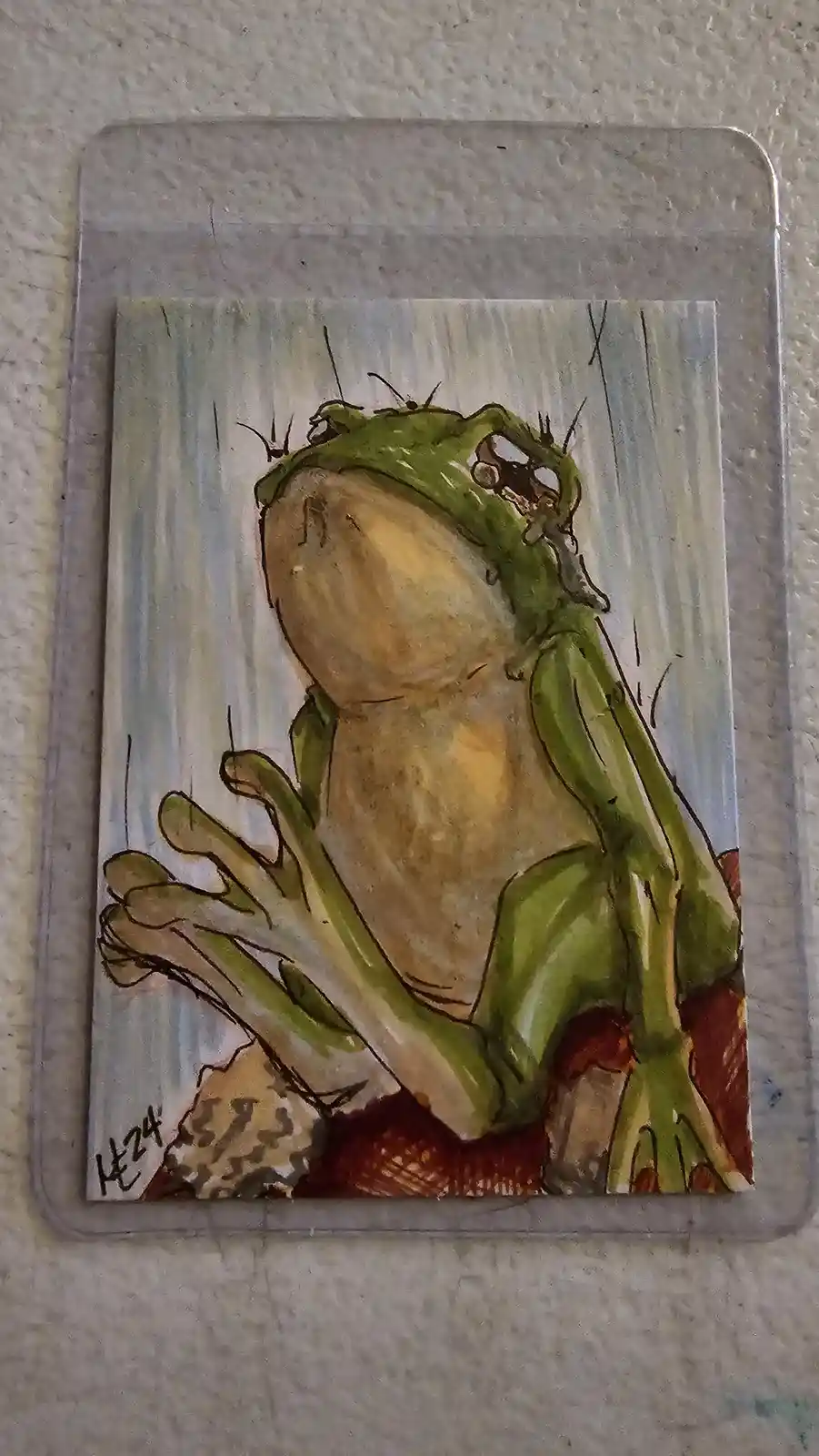A hand-drawn illustration of a green frog with a large, round belly, sitting on a rock and looking upward with a tear…