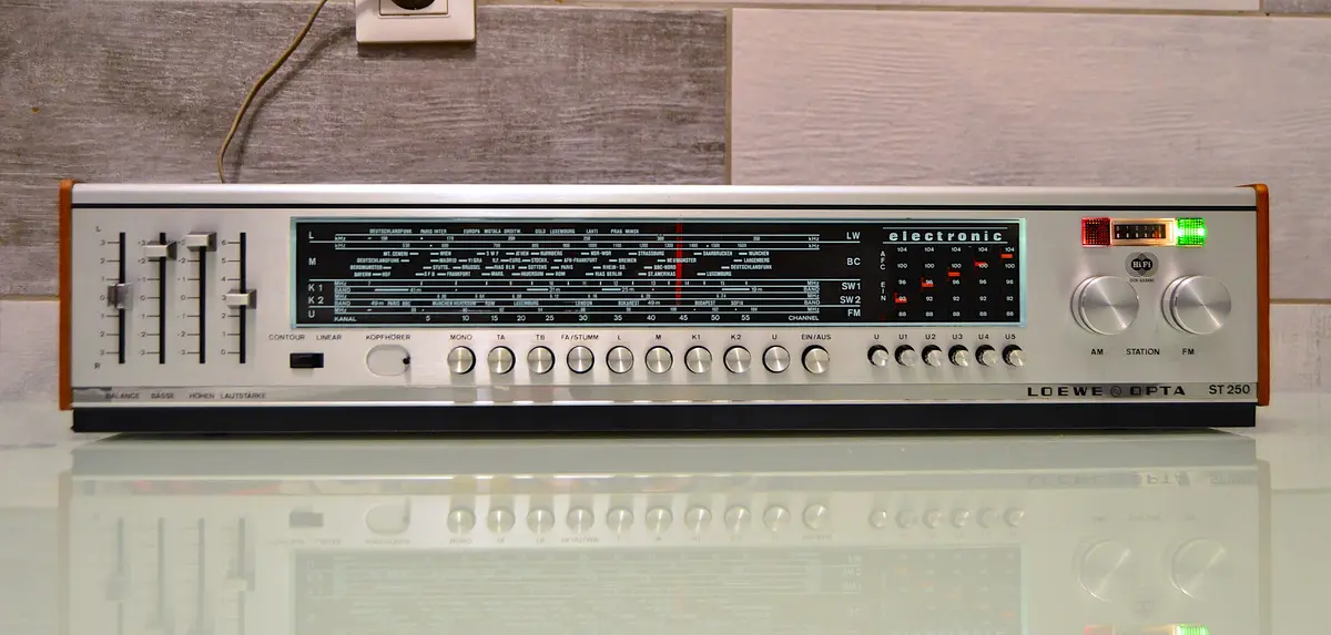 A vintage Loewe Opta ST 250 electronic radio receiver with a detailed display showing AM/FM frequencies and station names in…