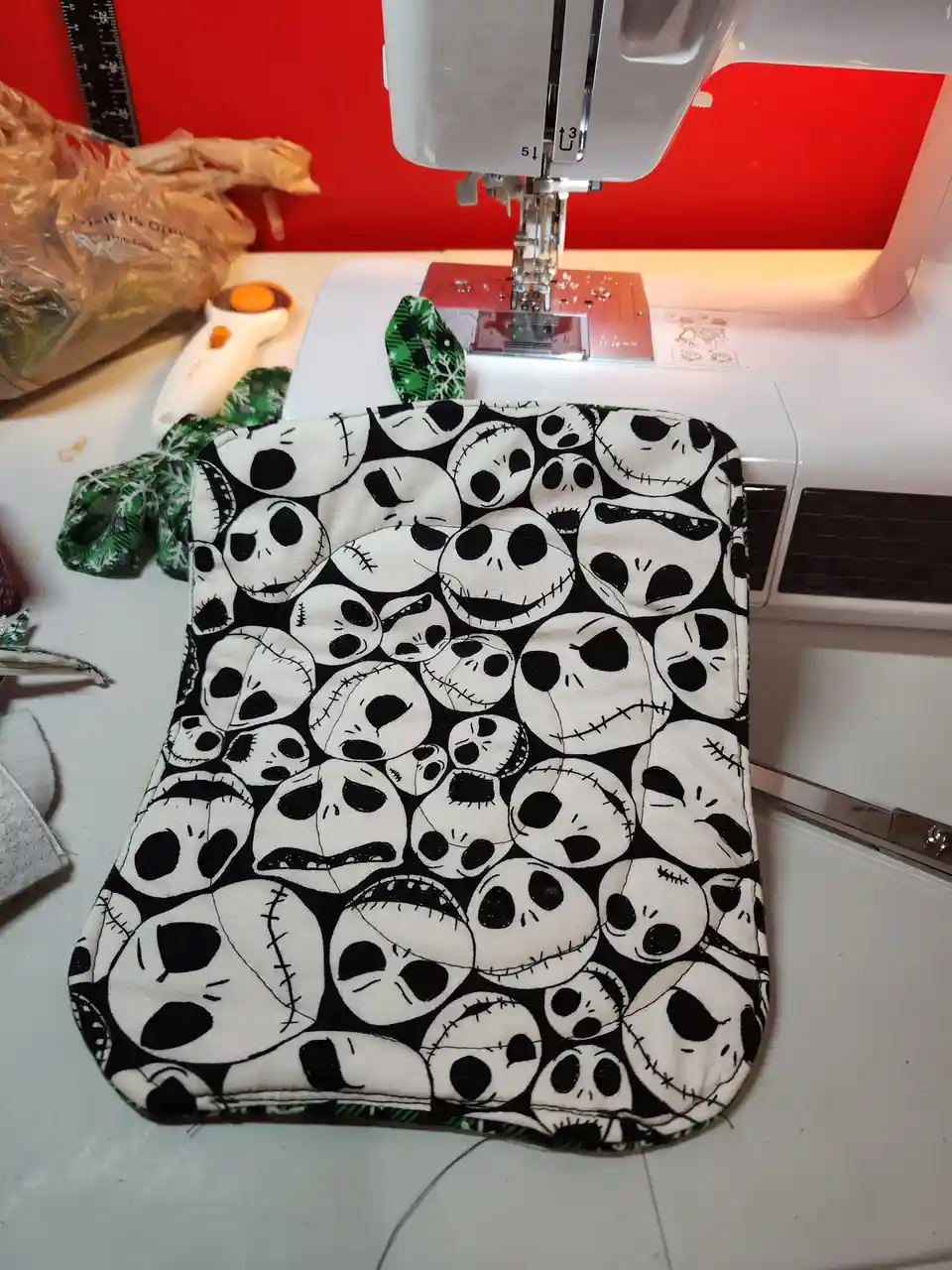 A handmade fabric item, likely a potholder or small pouch, covered in a repeating pattern of Jack Skellington's face from…