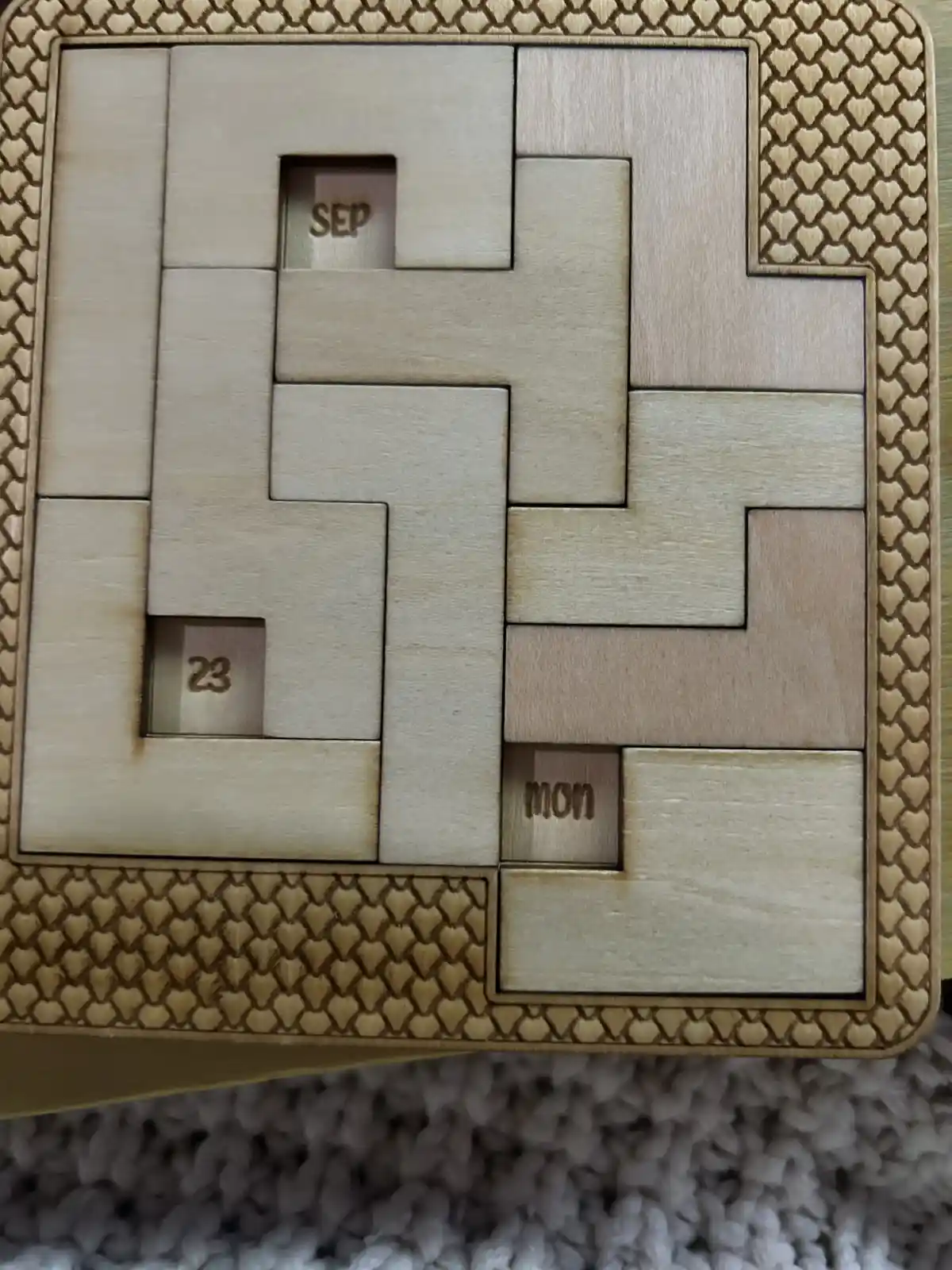 A wooden calendar puzzle with interlocking pieces, showing 'SEP' (September), '23' (the 23rd), and 'mon' (Monday) engraved…