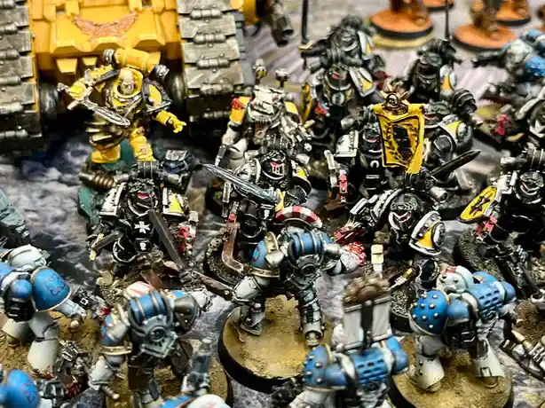 A close-up photo of numerous painted miniature warhammer 40k figurines, including yellow-armored space marines and…
