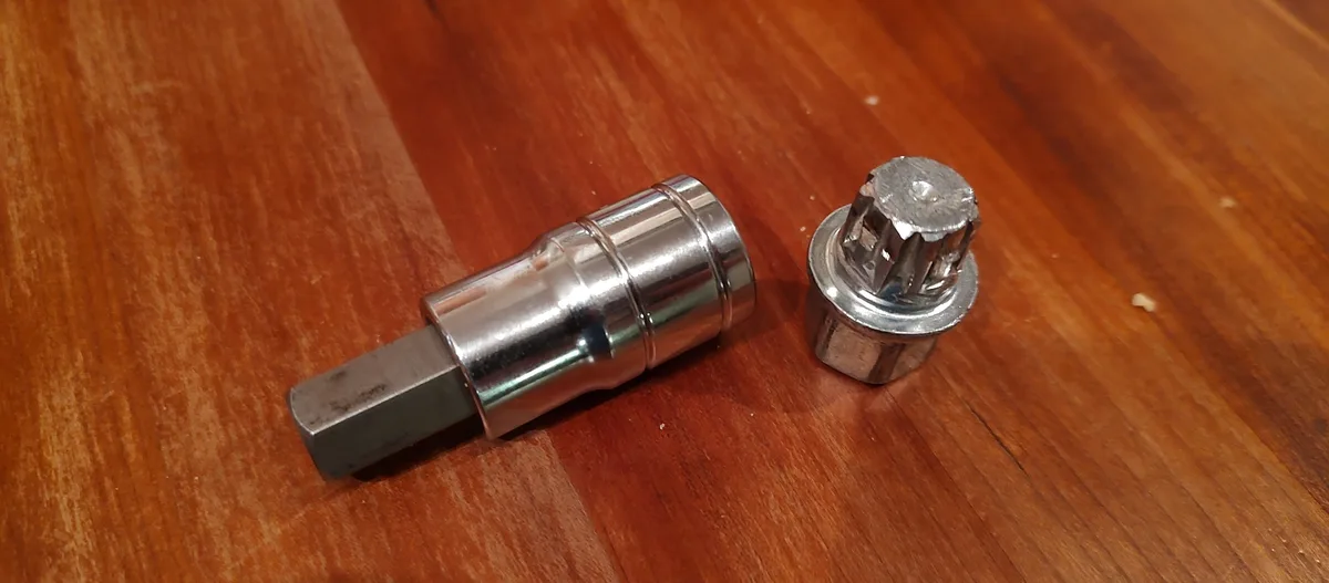 Two metal socket wrench components lie on a wooden surface: a cylindrical socket with a hexagonal drive end and a smaller…