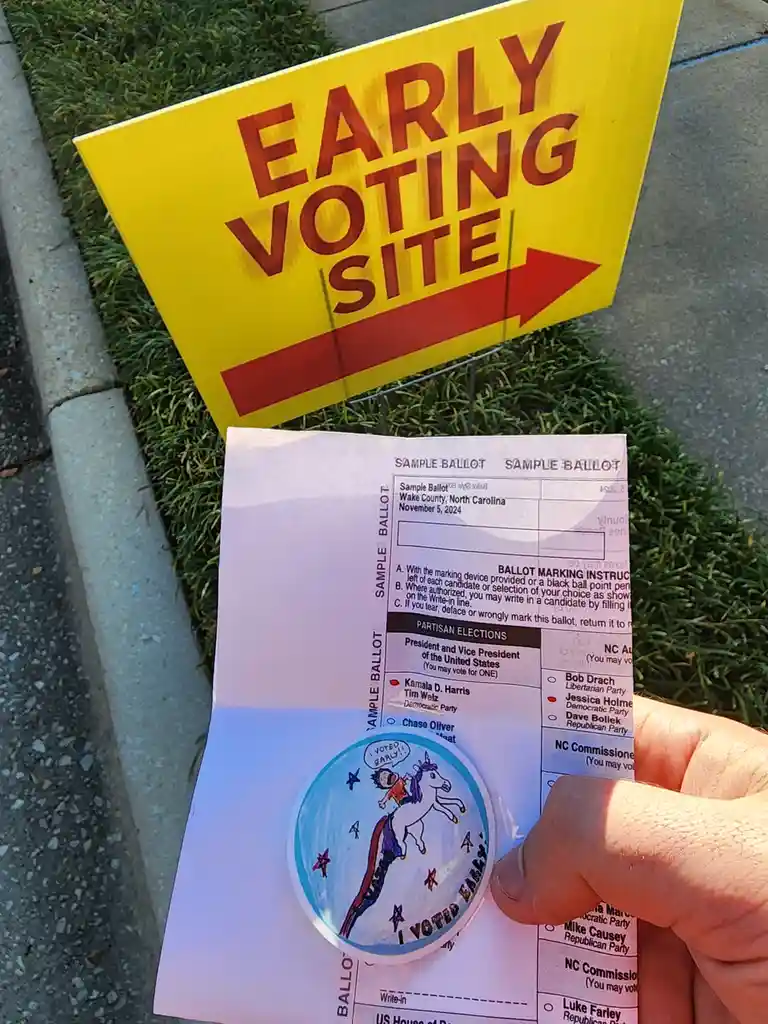 A hand holds a sample ballot from Wake County, North Carolina, dated November 5, 2024, with a circular sticker depicting a…