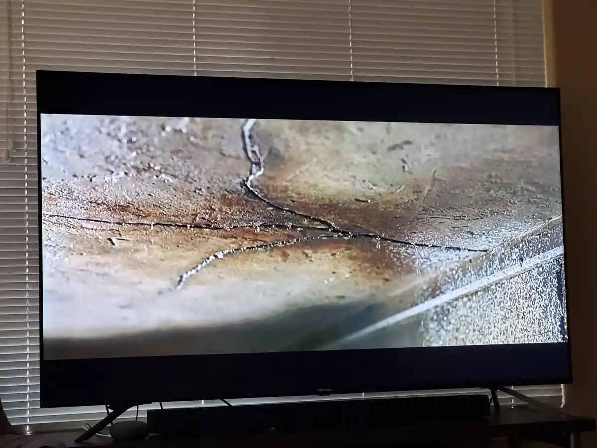A television screen displays a close-up of a cracked, wet concrete surface with water dripping from the fissures. The TV is…