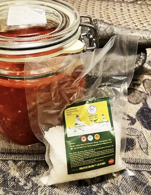 A glass jar filled with a red, chunky sauce sits next to a clear plastic bag of white salt labeled 'The Precious Treasure…