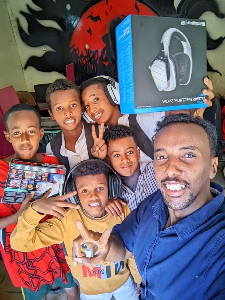 A man takes a selfie with five young boys, some wearing headphones and others holding a video game cartridge and a box of…