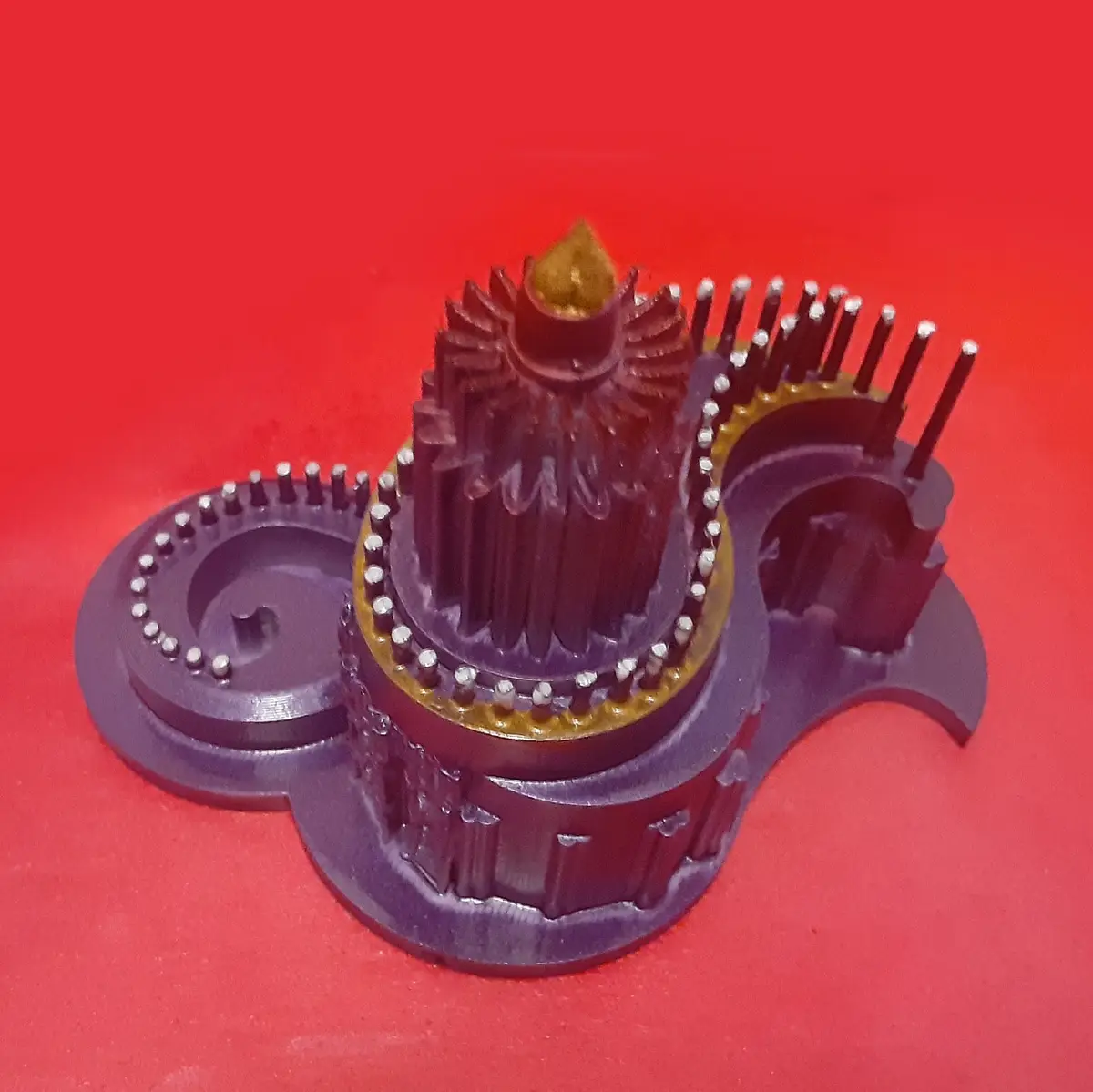 A 3d printed model of the Tower of Babel, intricately designed with gears, spires, and metallic accents, sits on a red…