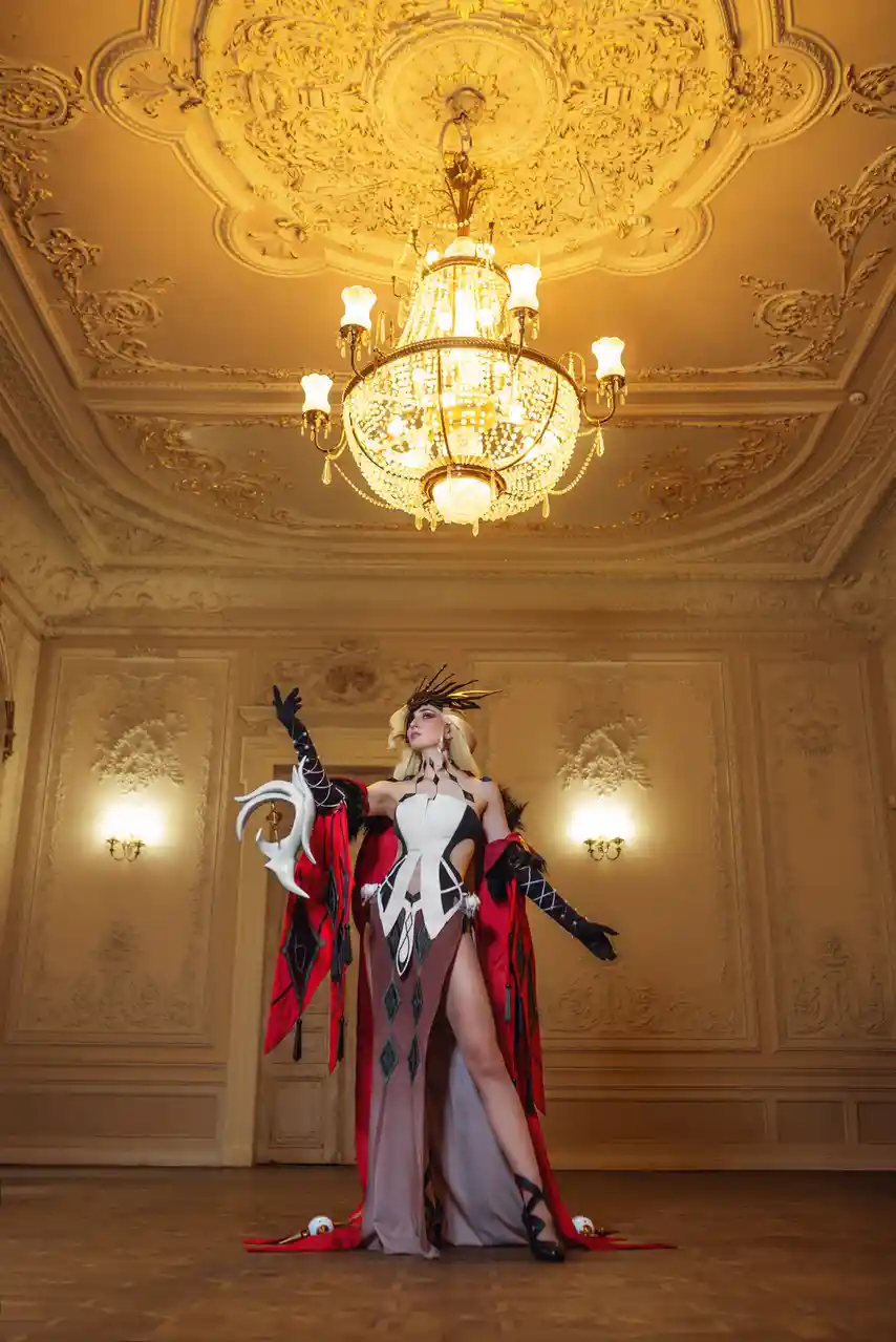 A cosplayer in an elaborate black, white, and red costume with a dramatic headdress and a large white horned prop stands in…