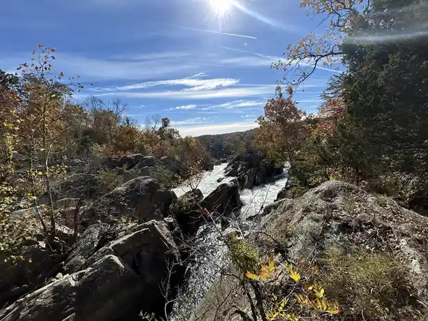 A scenic photo of a rocky river gorge in autumn with trees showing orange and yellow leaves under a bright blue sky with the…