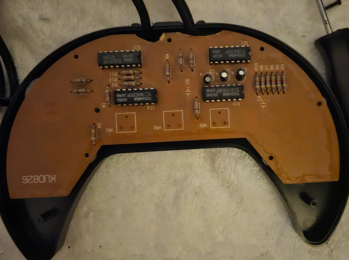 The image shows the underside of a disassembled video game controller, revealing its brown circuit board with various…
