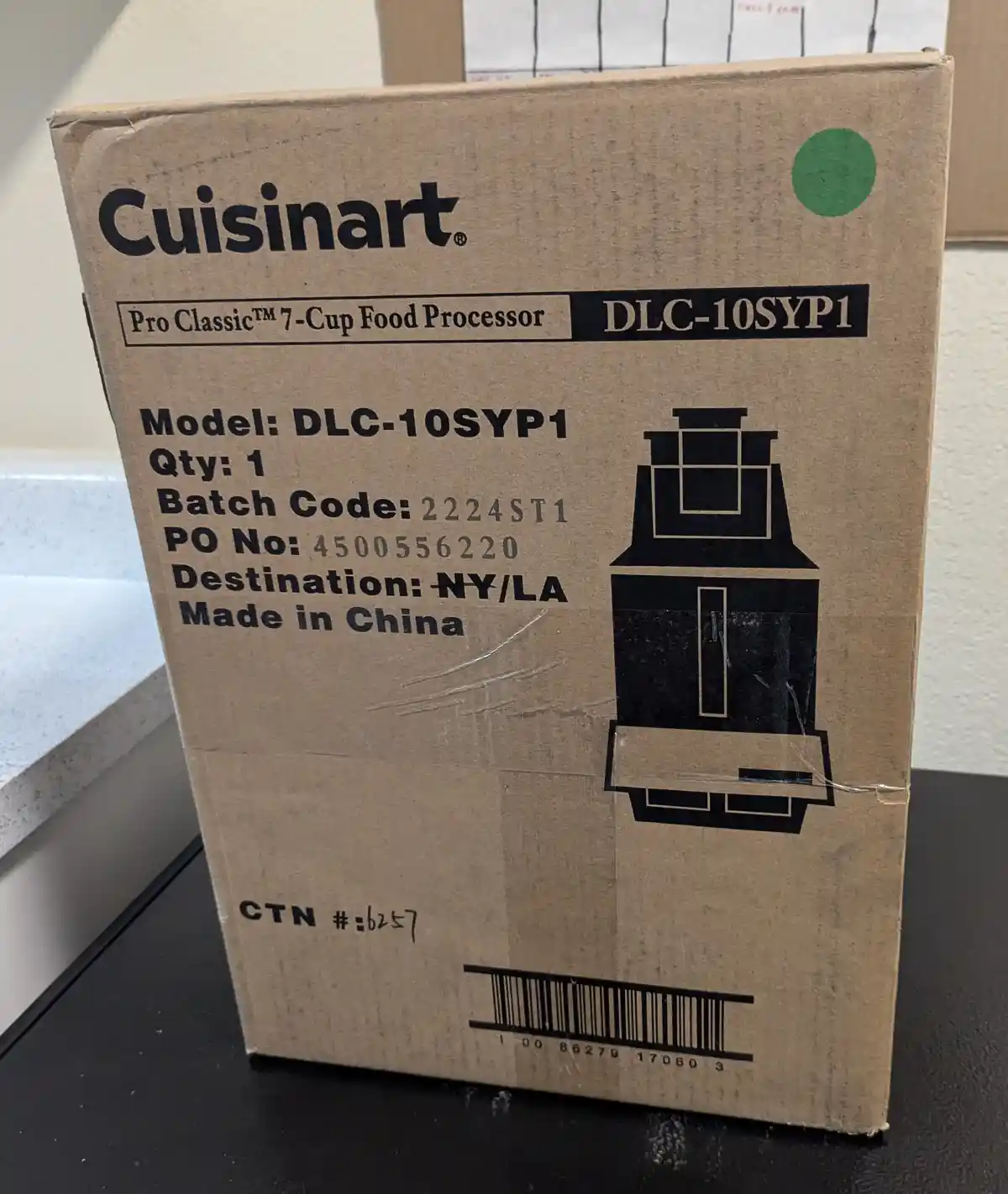 A brown cardboard box for a Cuisinart Pro Classic 7-Cup Food Processor (Model DLC-10SYP1) sits on a black surface. The box…